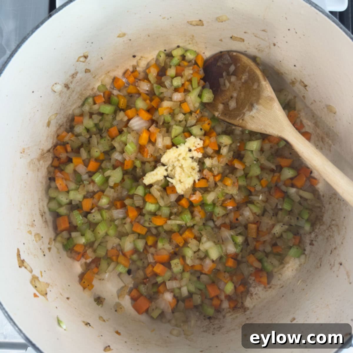 Rich Braised Beef Short Rib Ragu 6 Carrots, onion, celery and garlic cooking in a pot with wooden spoon.