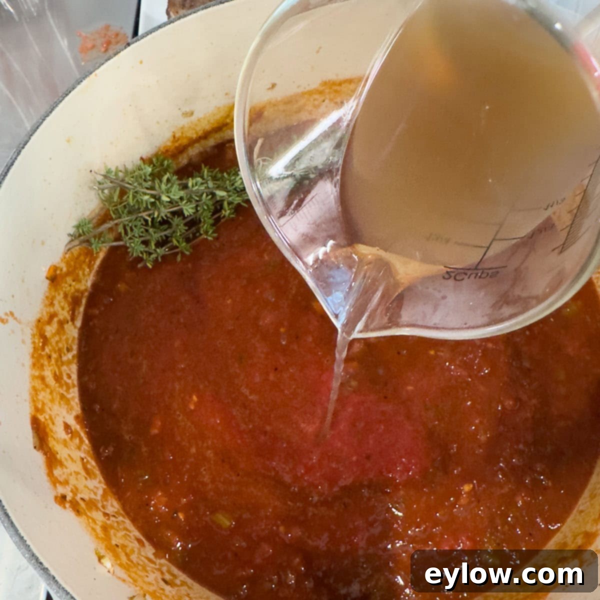Rich Braised Beef Short Rib Ragu 10 Broth being poured into a pot with vegetables and tomatoes.