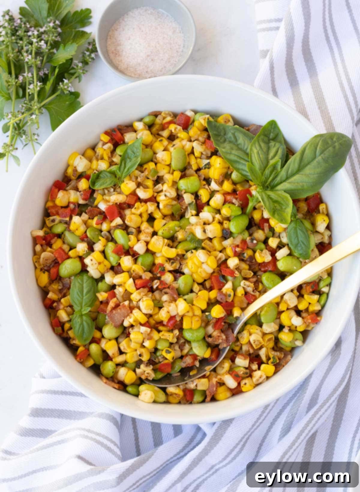 A colorful bowl of sweet corn succotash with bacon, yellow, red and green in a white bowl.