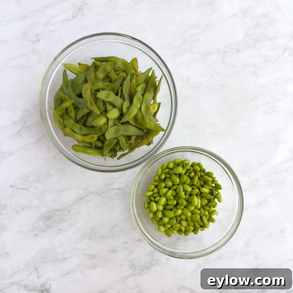 Shelled edamame and spent pods in glass bowls.