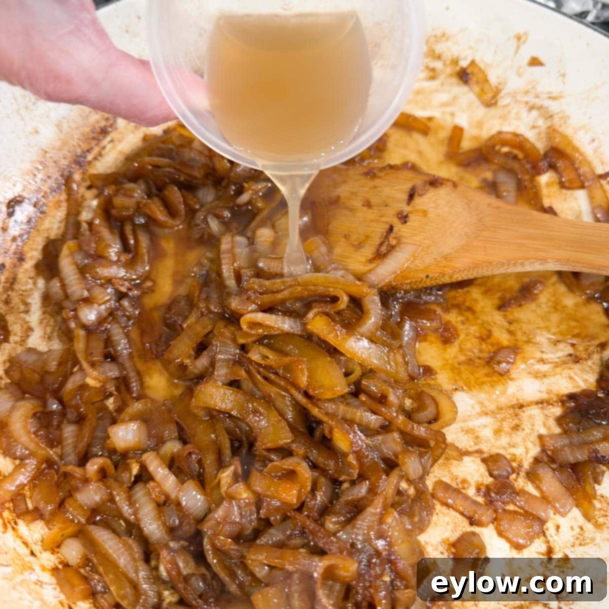 Adding beef broth to a pan of richly caramelized onions to create a savory sauce.