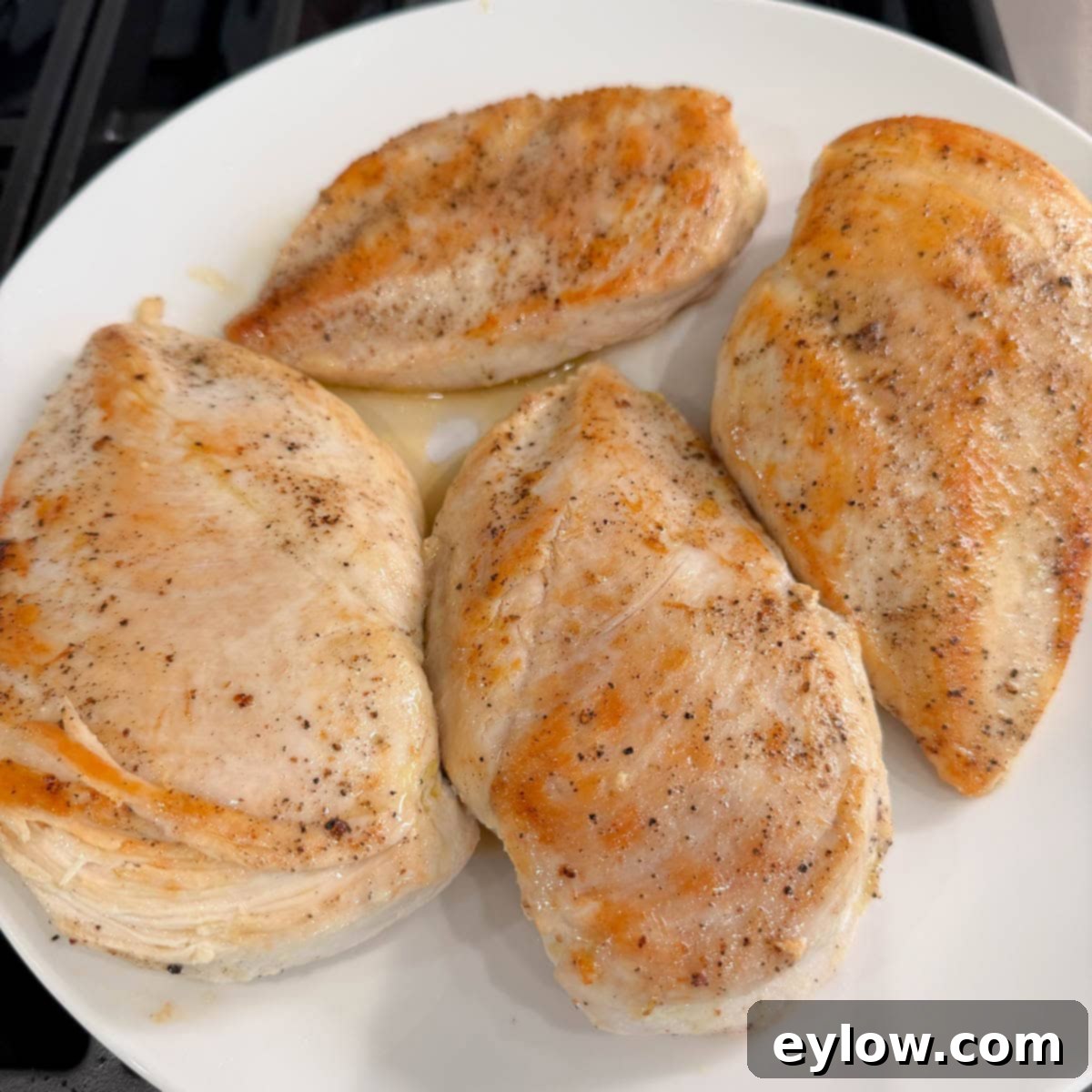 Browned chicken breasts resting on a white plate, covered with foil to keep warm, on a stovetop.
