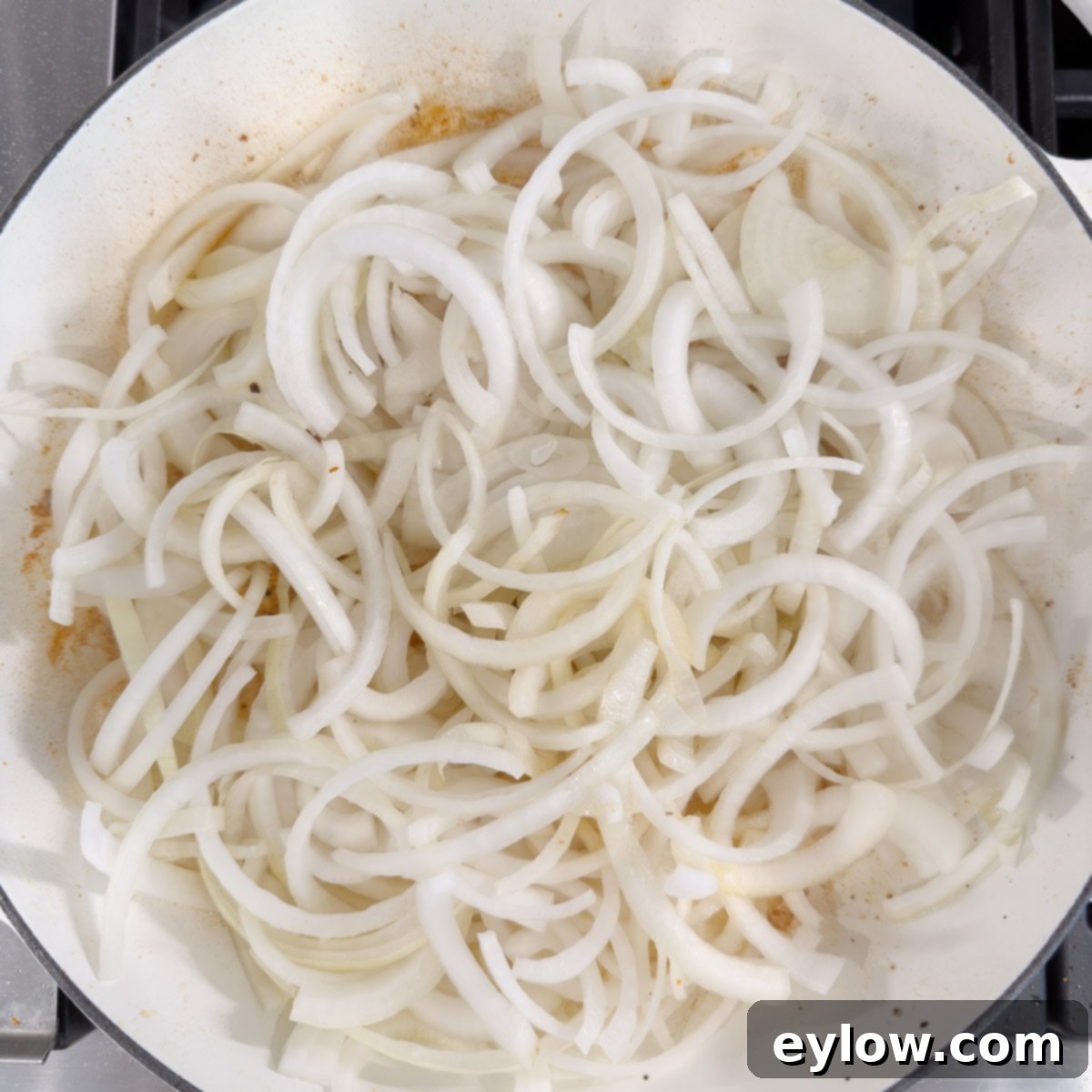 A pan full of thinly sliced onions beginning the caramelization process with melted butter over medium-low heat.