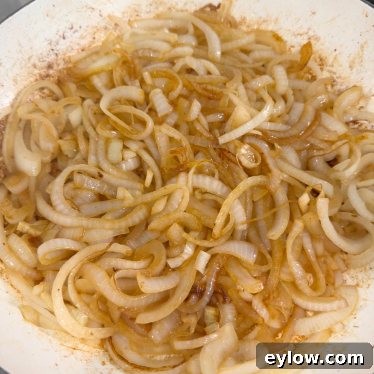 Light golden caramelized onions in a round shallow pan, midway through the cooking process.