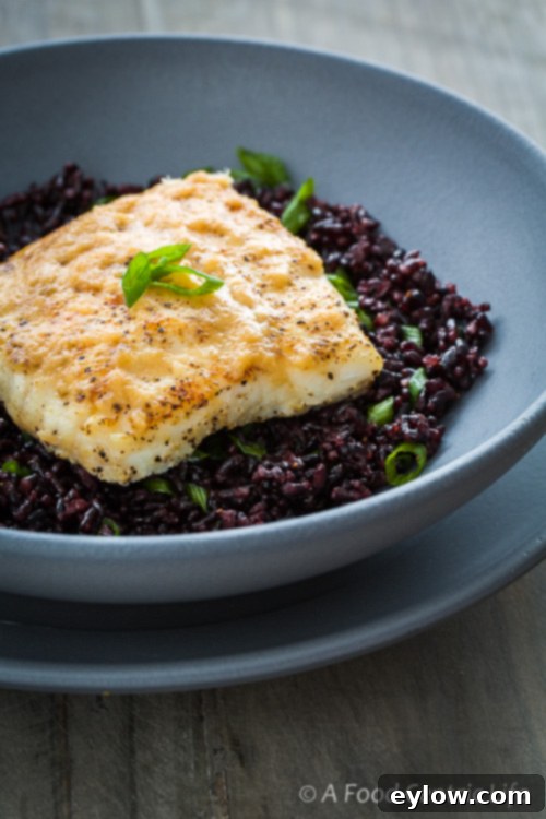 Golden halibut in a gray bowl on black rice with miso butter sauce. 