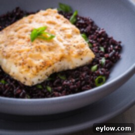 Miso butter topped halibut on a bed of black rice in a gray bowl.