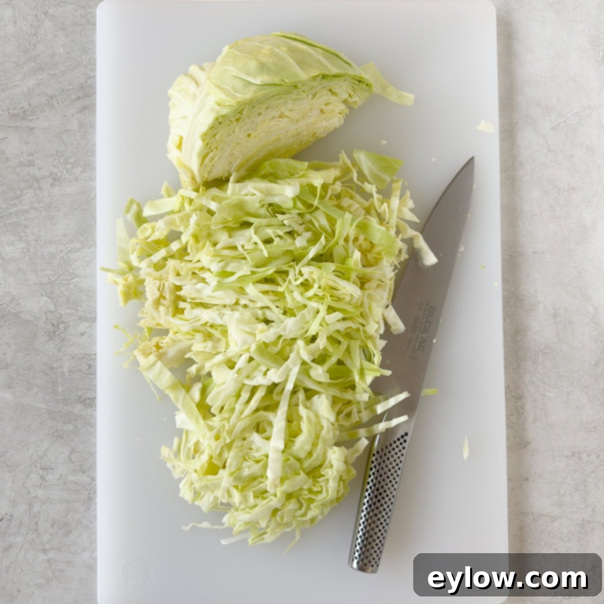 Thinly slicing cabbage on a white cutting board with a chef's knife.