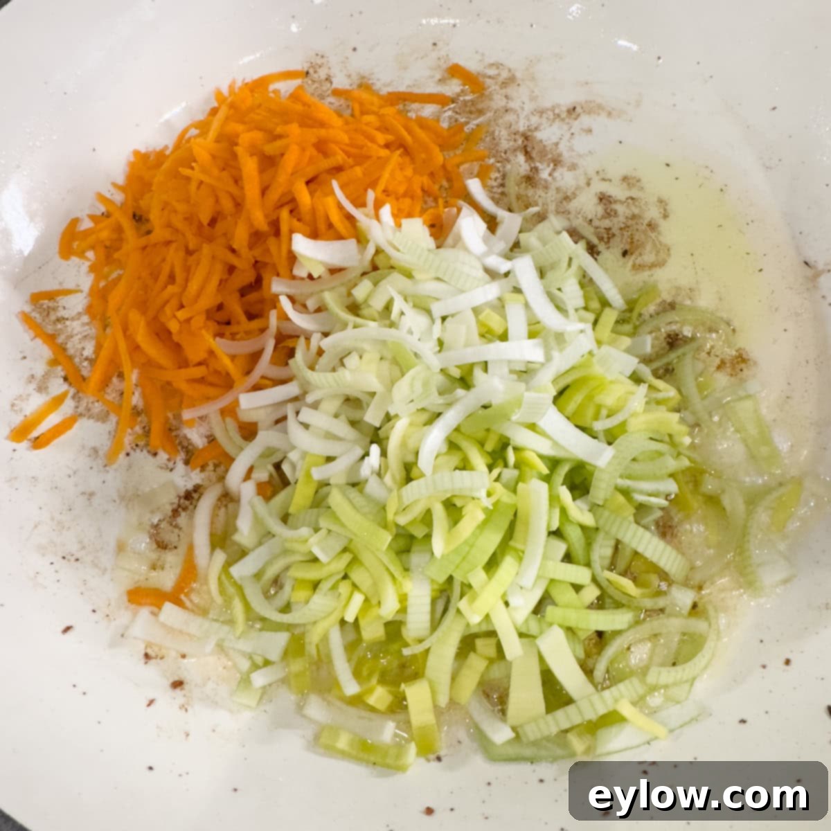 Raw grated carrot and leek in a saute pan starting to cook.