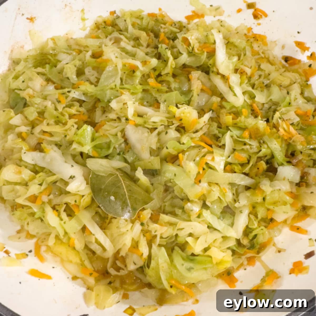 Cooked green cabbage, orange carrots, and leek in a saute pan. 
