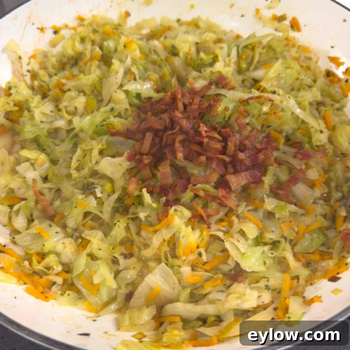 Cooked green cabbage in a pan with the addition of crispy bacon.