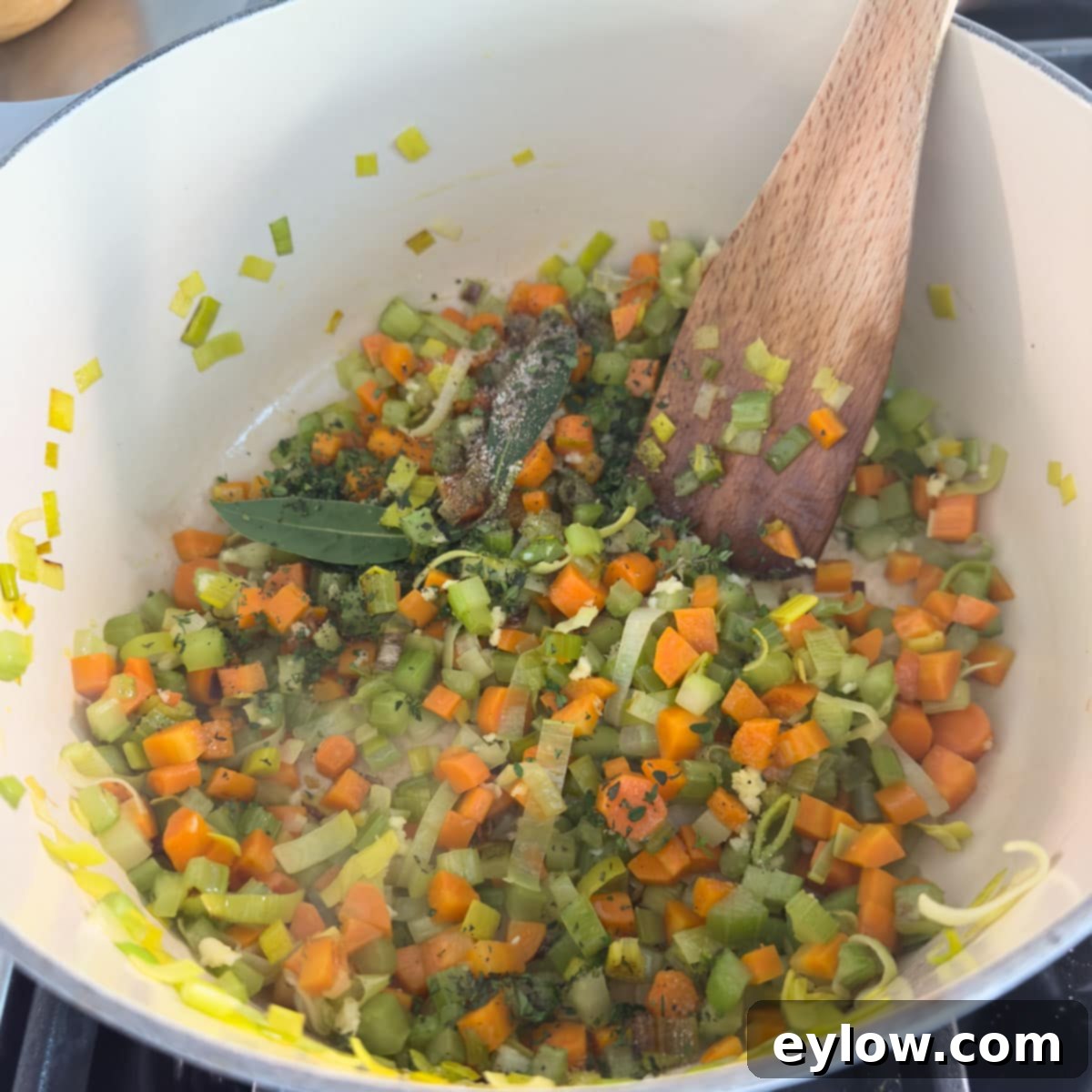 Chopped vegetables, including onions, carrots, and celery, actively sautéing in a Dutch oven on a stovetop for chicken vegetable soup.