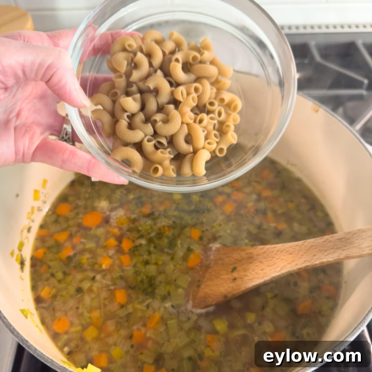 Elbow macaroni pasta being added to a simmering pot of chicken vegetable soup.