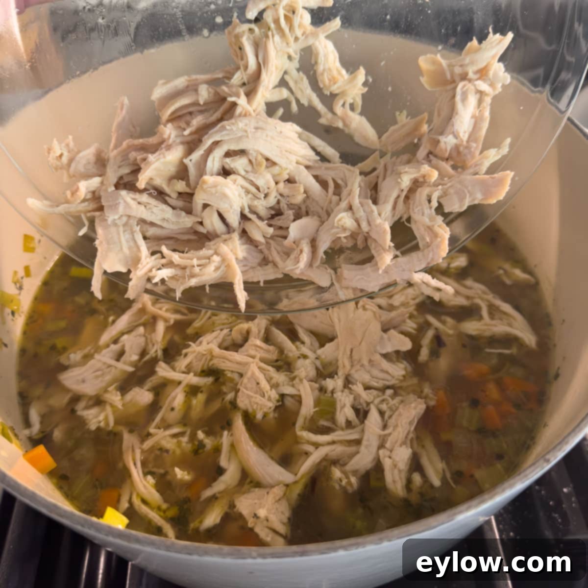 Shredded chicken being added back into a pot of simmering chicken vegetable soup with pasta.