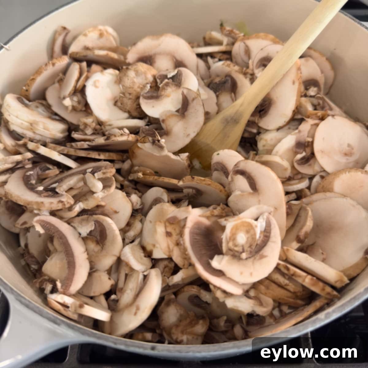 A pot full of raw sliced mushrooms beginning to cook down with the aromatics for soup.