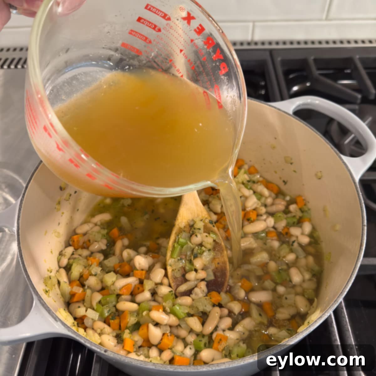 Pouring golden broth into a pot while making soup. 