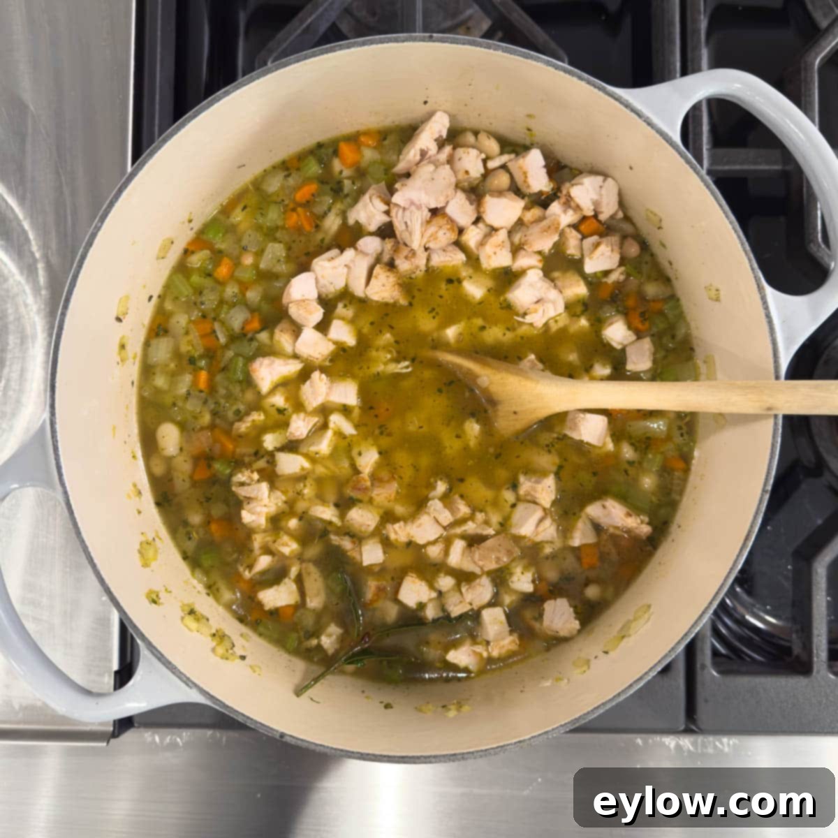 Adding chopped chicken to a pot for white bean soup.