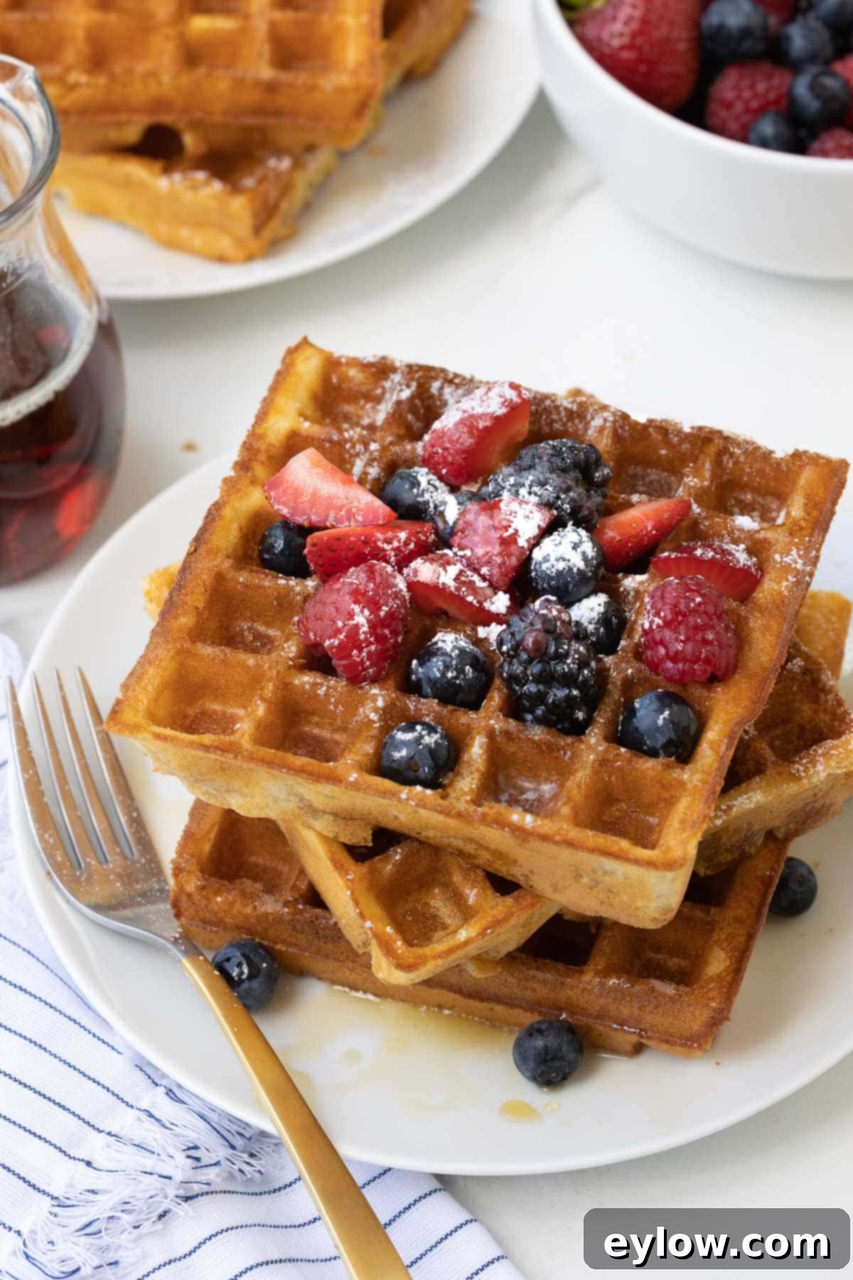Fluffy Gluten-Free Waffles 2 A stack of golden crispy gluten-free waffles with berries, maple and powdered sugar.