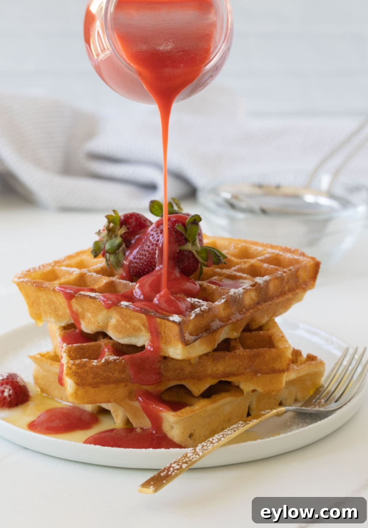Fluffy Gluten-Free Waffles 11 Golden gluten-free waffles with melted butter and strawberry sauce poured over the top.