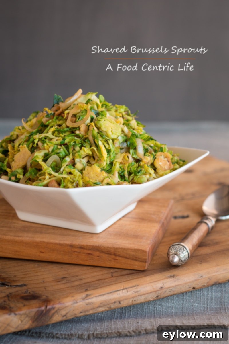 A beautifully presented white bowl of warm Brussels sprouts salad, generously garnished with crispy bacon and sautéed shallots, rests invitingly on a rustic wooden table. The dish exudes warmth and freshness, ready to be enjoyed.