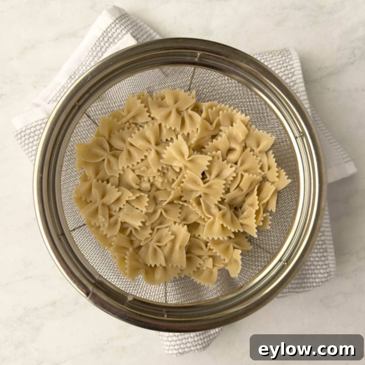 Drained butterfly pasta in a strainer on a gray towel.