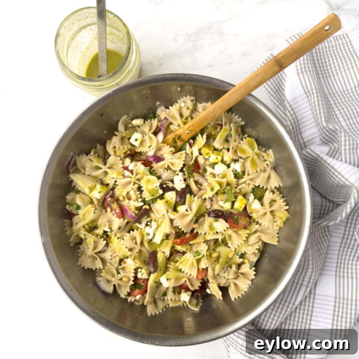 Mixing pasta salad in a large steel bowl with dressing.