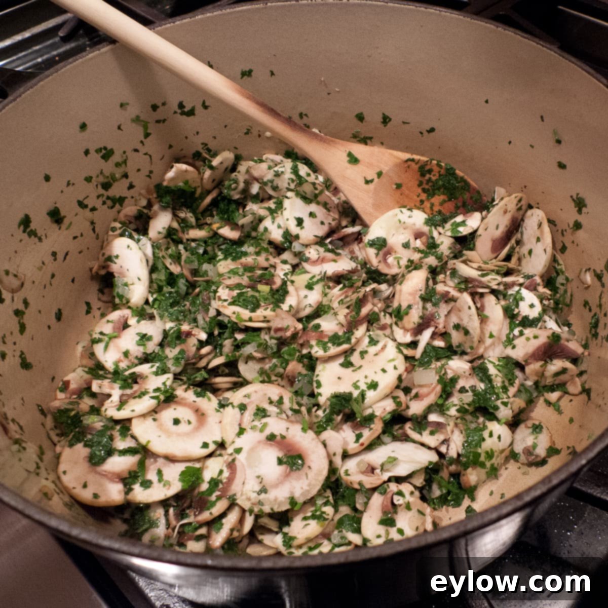 Sliced mushrooms and chopped herbs in a large pot cooking for pasta sauce.