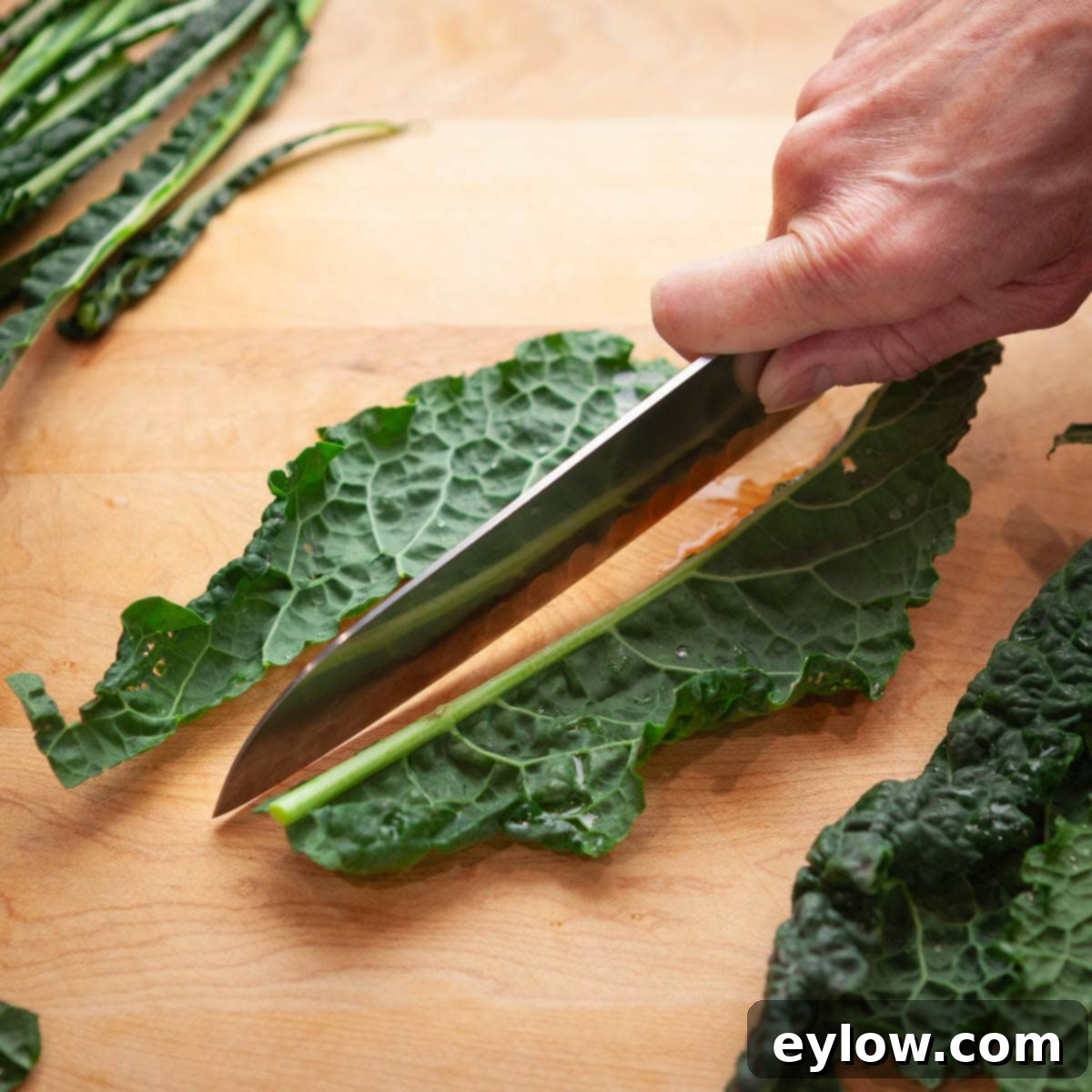 Slicing the tough center ribs from kale leaves on a cutting board.