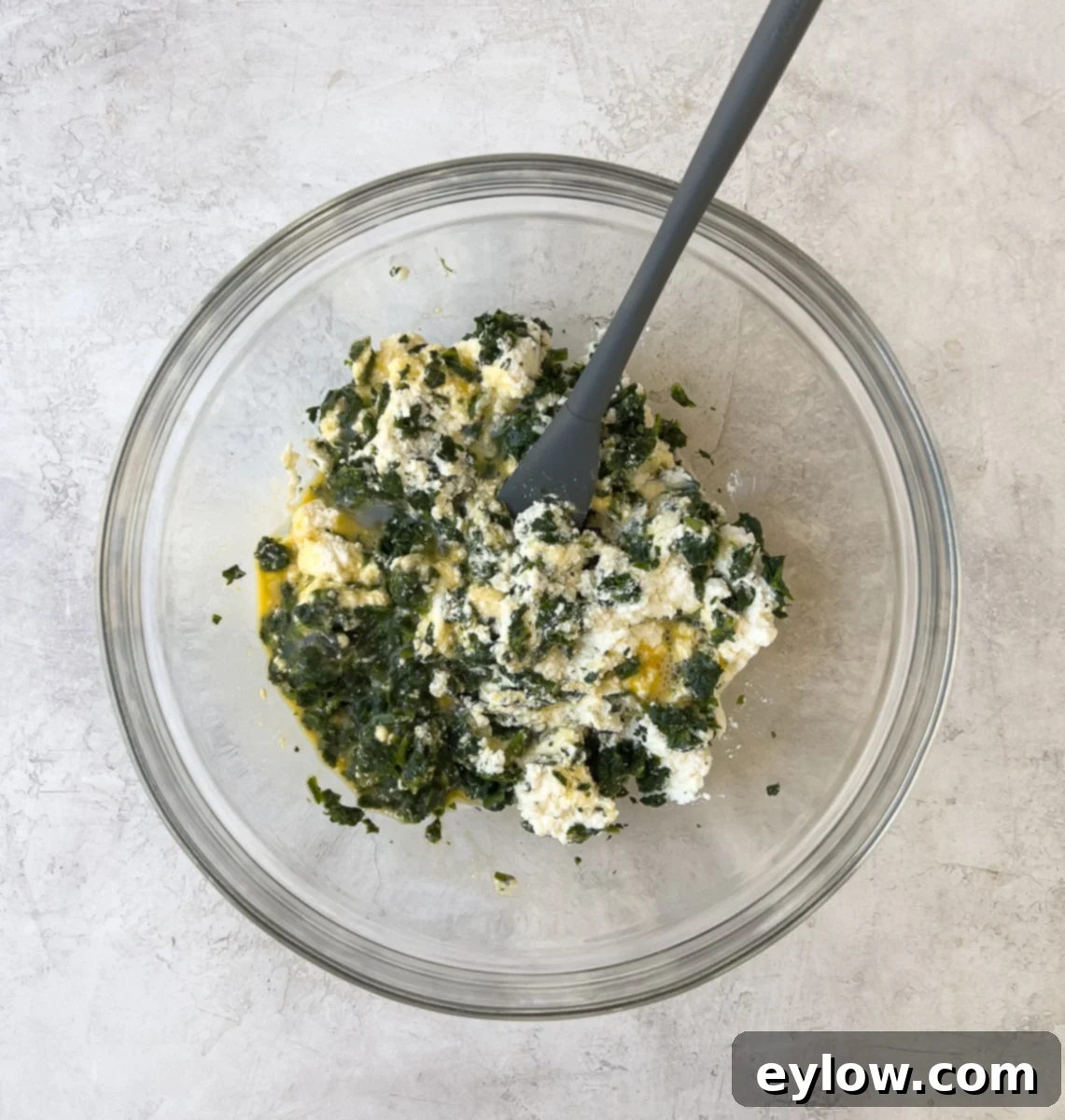 Greens, ricotta, eggs, cheese, and spices in a glass bowl for ricotta filling.