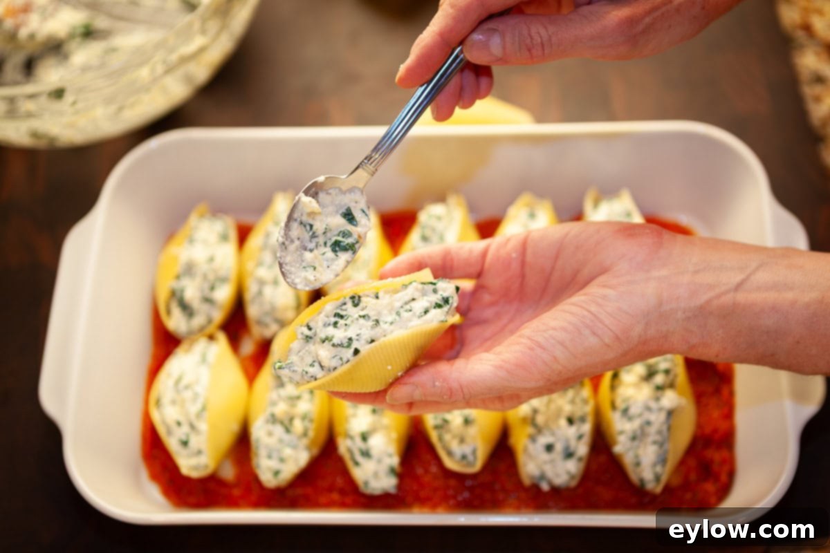 A white casserole dish of pasta shells stiffed with ricotta and kale getting ready to bake.