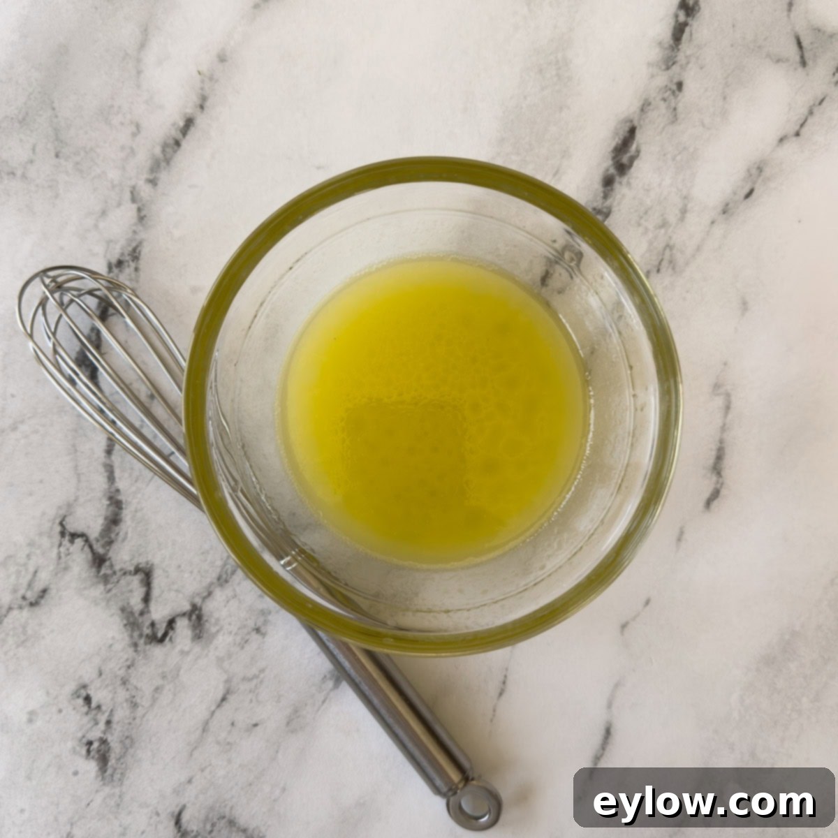 Crisp Cucumber Dill Feta Medley 7 A glass bowl of lemon vinaigrette with a silver whisk on a marble counter.