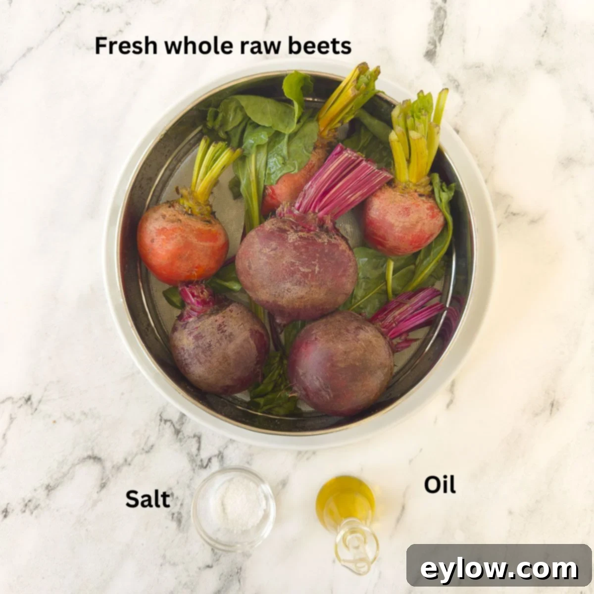 Fresh red and golden beets, olive oil, and salt on a white surface.