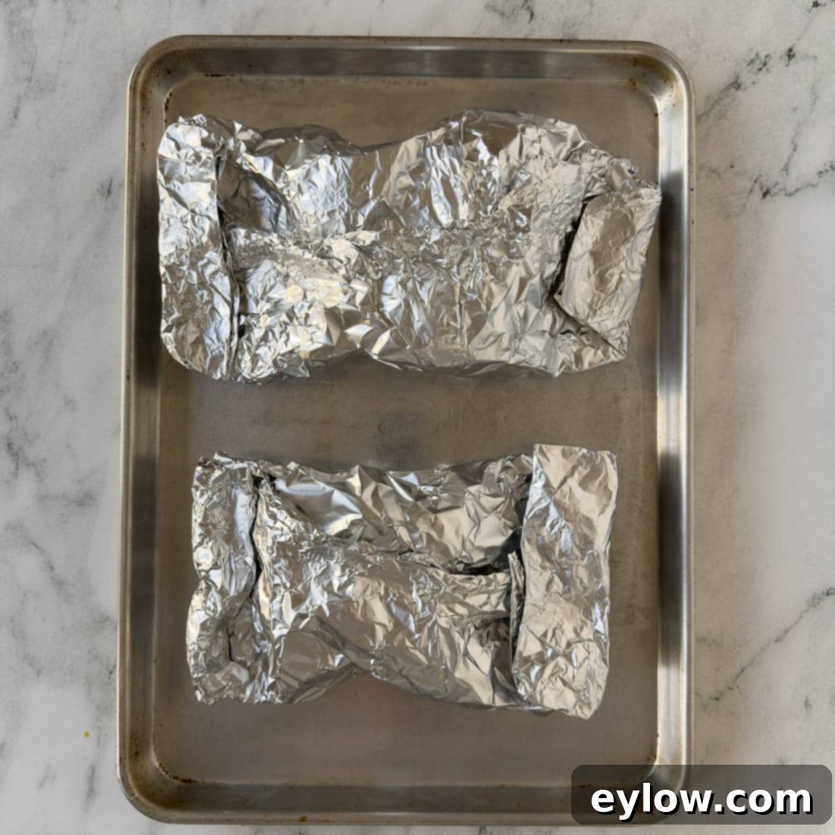 Aluminum foil packets on a rimmed baking sheet on the counter. 