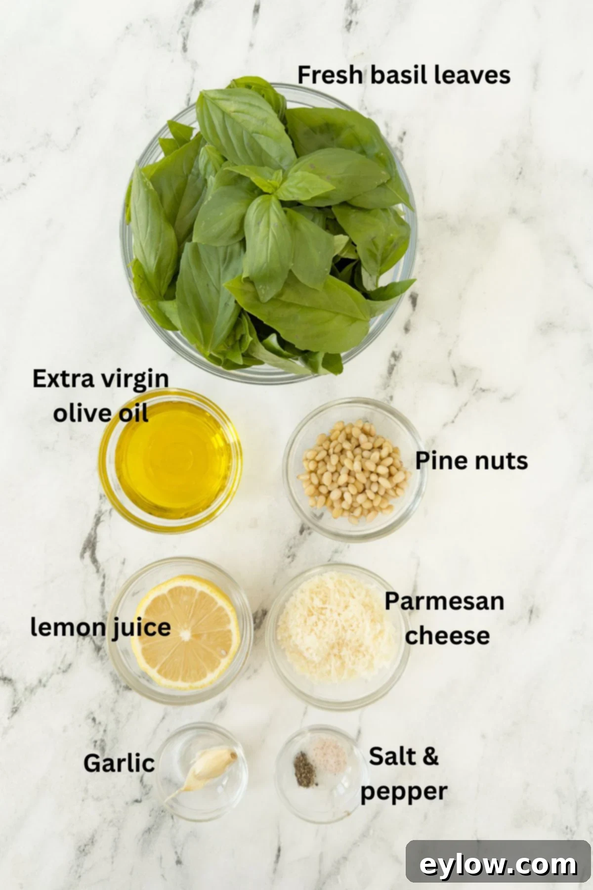 Genovese Basil Pesto: The Original Italian Recipe 3 A curated display of fresh ingredients for basil pesto (pesto alla Genovese) meticulously arranged in clear glass prep bowls on a rustic kitchen counter, ready for blending.