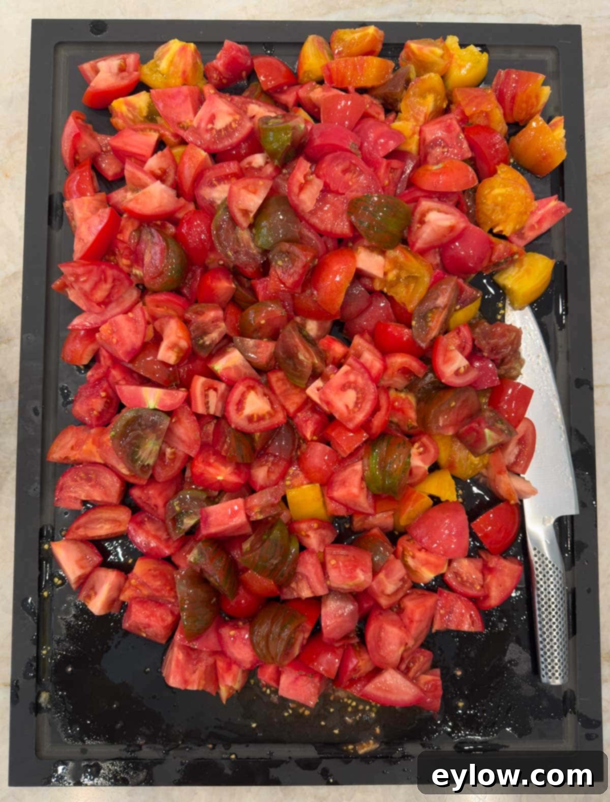 Ten pounds of colorful chopped tomatoes on a black cutting board with a knife.