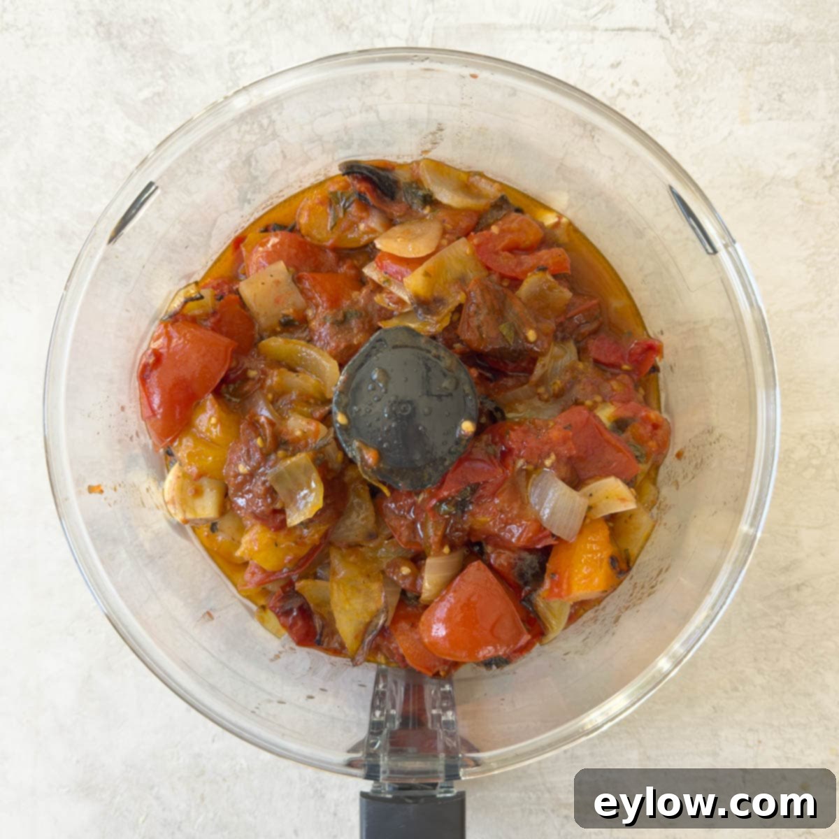 Roasted tomatoes, onions, garlic cloves, and herbs in a food processor to be pureed.
