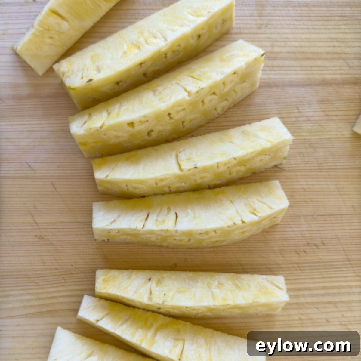 Cleaned pineapple spears, free of skin and core, neatly arranged on a cutting board, ready for the final chopping stage.
