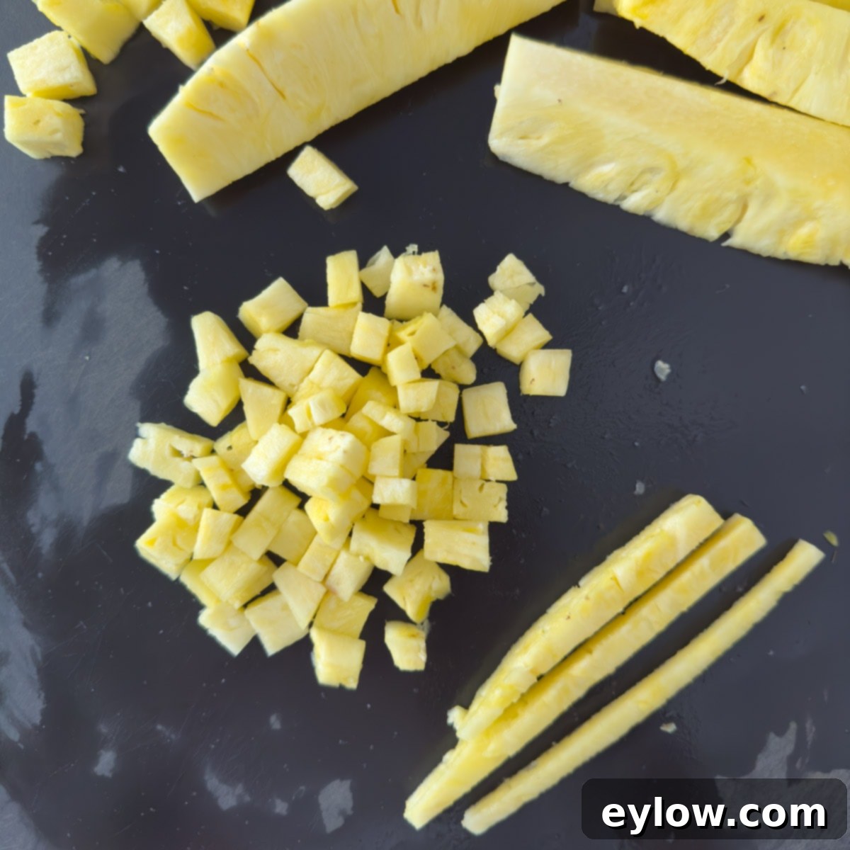Finely diced yellow pineapple pieces neatly arranged on a black cutting board, ready for a tropical salsa.