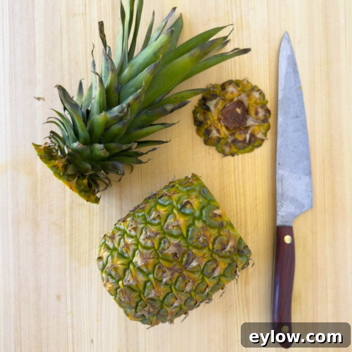 A pineapple on a cutting board, with its crown and base already removed, preparing for vertical cuts.