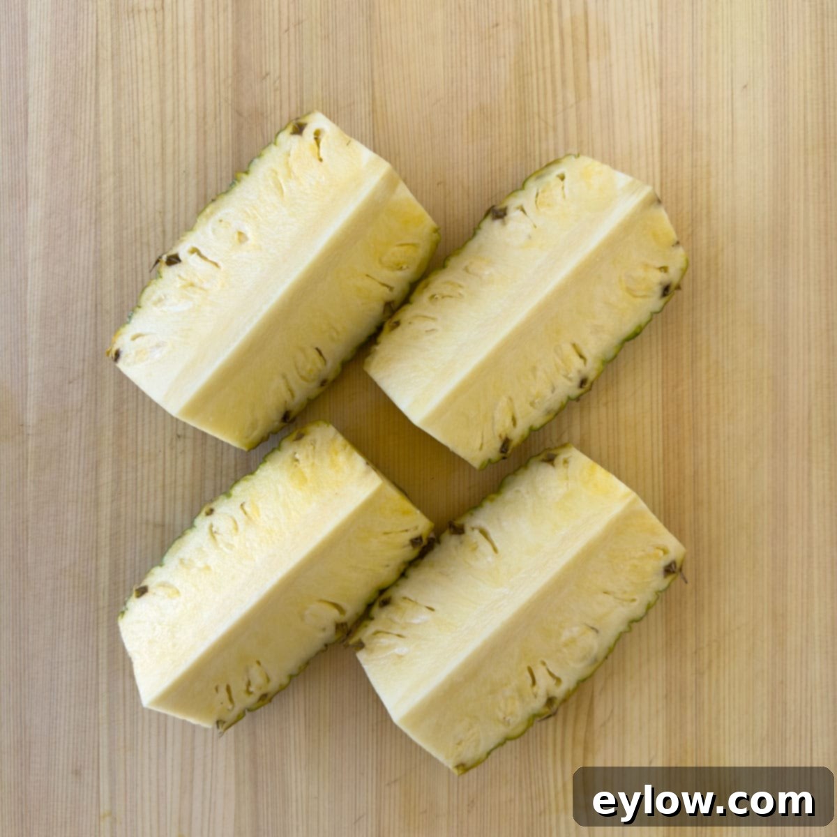 Two pineapple halves on a cutting board, one cut into quarters, showing the next step in preparation for salsa.