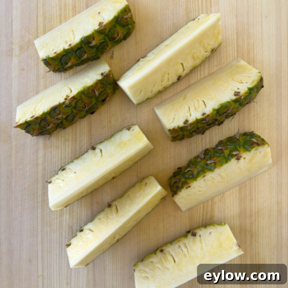 Pineapple quarters on a cutting board, one cut into eighths, demonstrating the next division for easy processing.