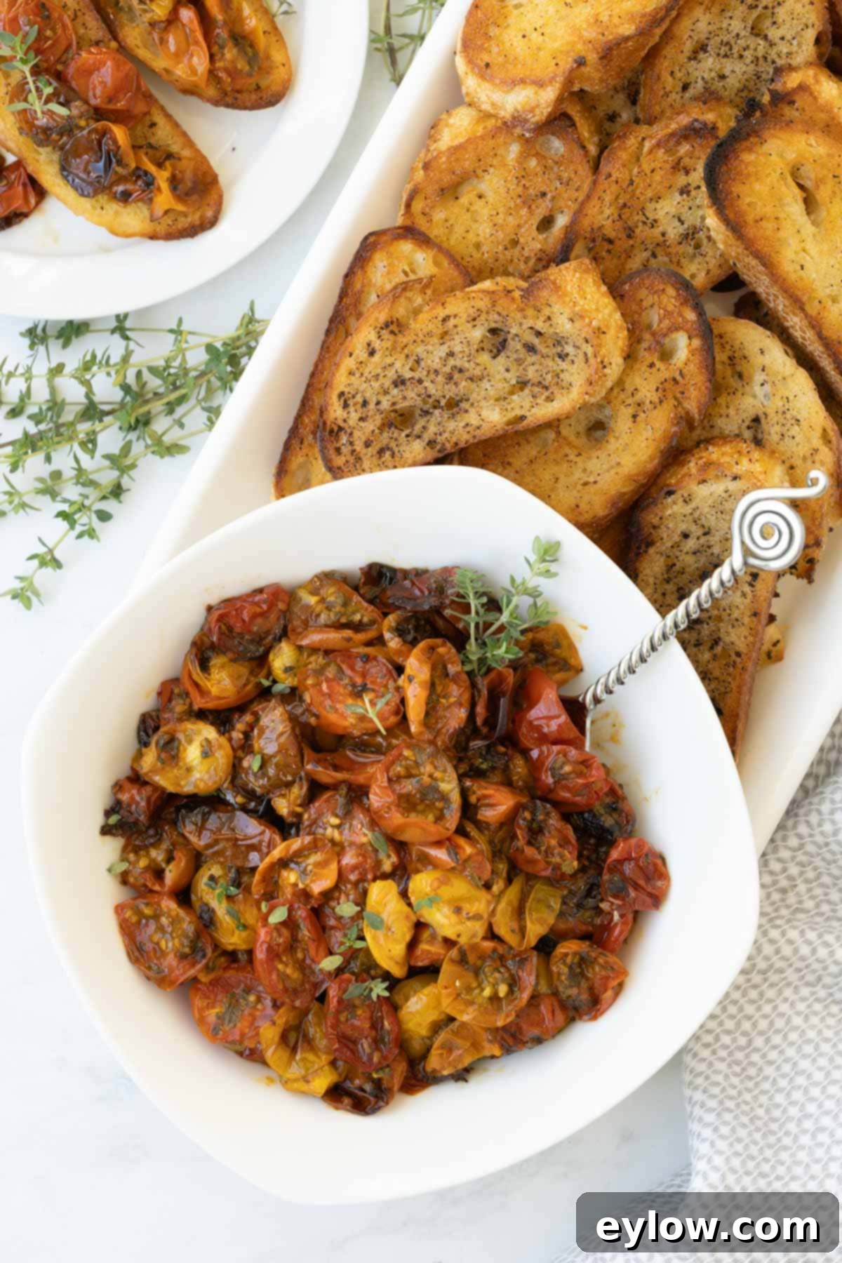 Aromatic Garlic and Thyme Roasted Tomatoes 2 A bowl of colorful oven roasted tomatoes with thyme leaves and golden crostini. The tomatoes are plump and glistening, showcasing their jammy texture and vibrant hues.