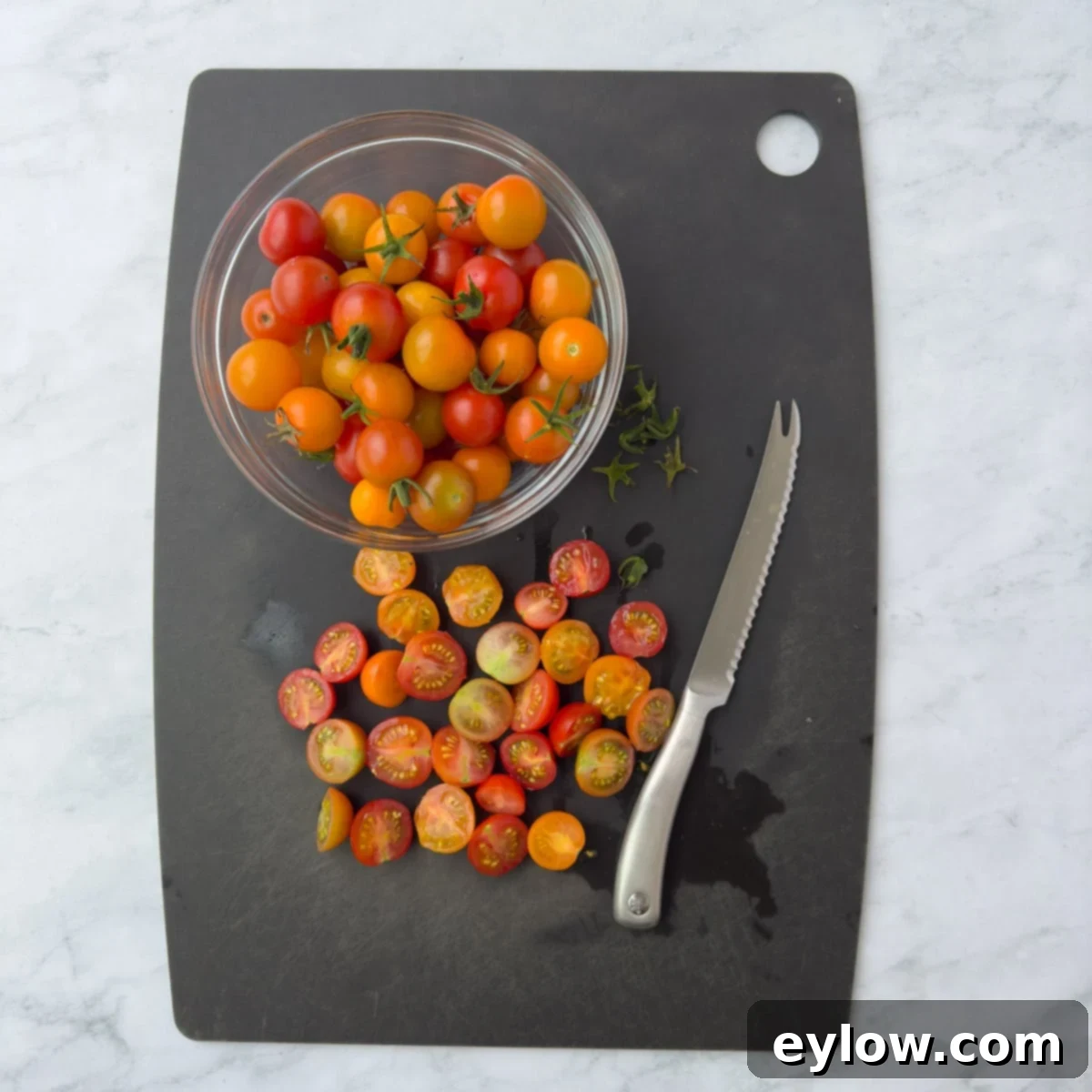 Aromatic Garlic and Thyme Roasted Tomatoes 4 Cutting cherry tomatoes in half for roasting on cutting board. A knife is shown slicing through a plump red cherry tomato.
