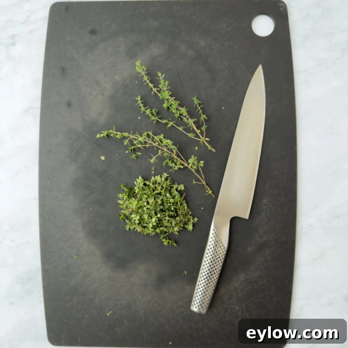 Aromatic Garlic and Thyme Roasted Tomatoes 5 Chopping fresh thyme leaves on a cutting board. A small pile of fragrant green thyme leaves is ready for use.