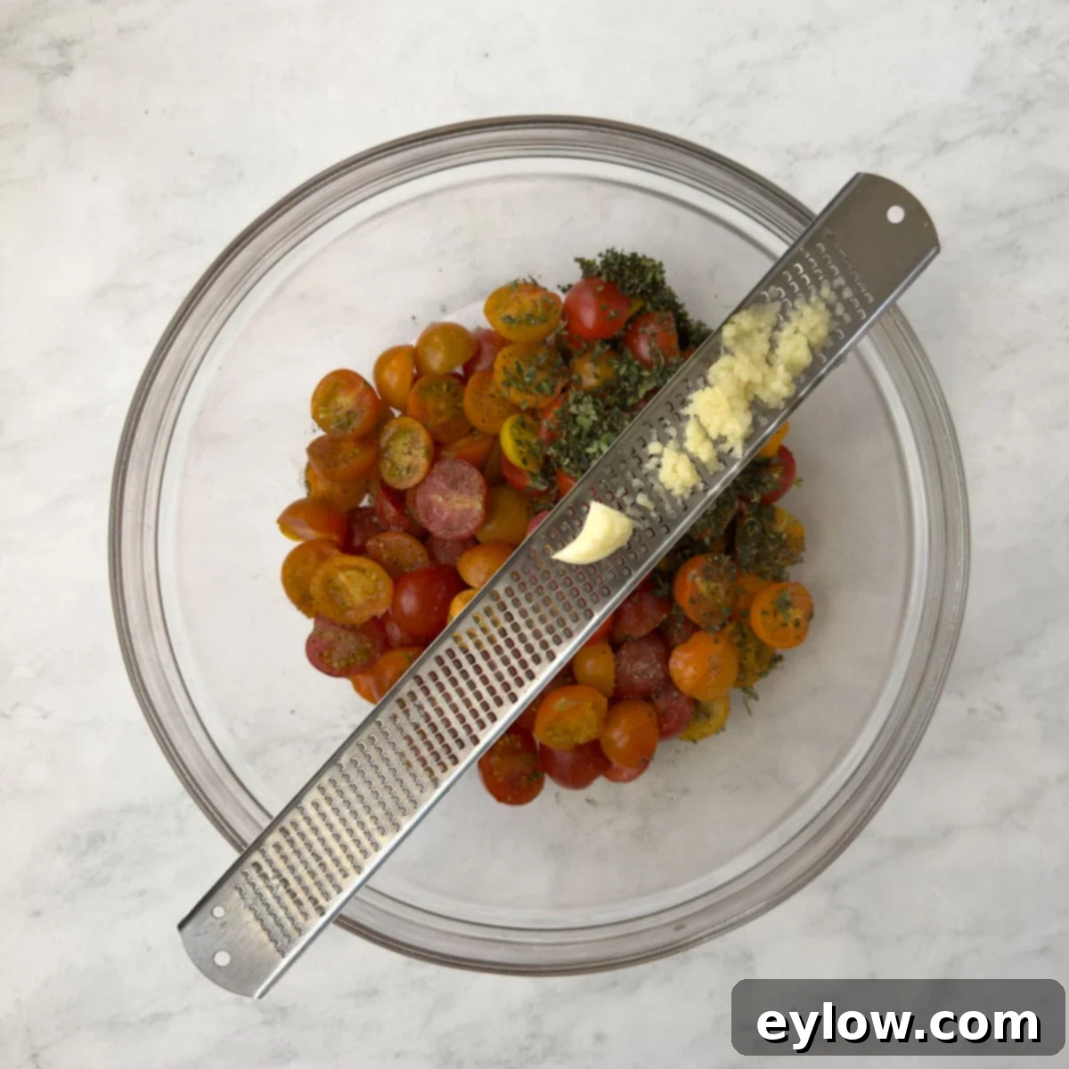 Aromatic Garlic and Thyme Roasted Tomatoes 6 Zesting garlic fine into a bowl of cherry tomatoes for roasting. A microplane grater is held over a bowl, with garlic being finely grated directly onto the tomatoes.