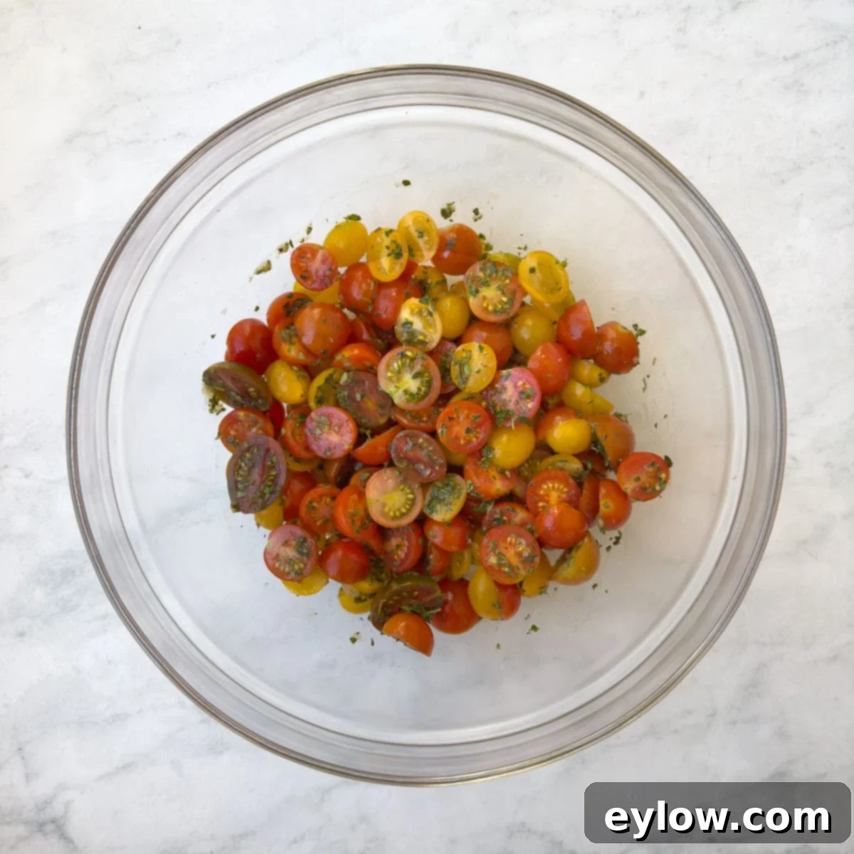 Aromatic Garlic and Thyme Roasted Tomatoes 7 A glass bowl filled with colorful cherry tomatoes tossed with herbs and garlic, glistening with olive oil.