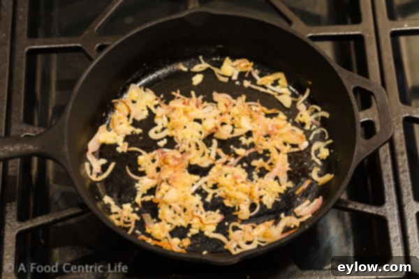 Close-up of thinly sliced shallots and minced garlic sautéing in butter, forming the aromatic base for the mushroom dish.