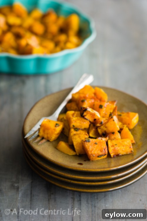 A portion of golden-roasted butternut squash garnished with fresh sage on a rustic white plate, set on a wooden table.