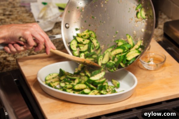 Golden Parmesan Zucchini Gratin 4 A chef is pouring cooked, slightly browned zucchini into a shallow oval casserole dish, preparing it for baking under the broiler.