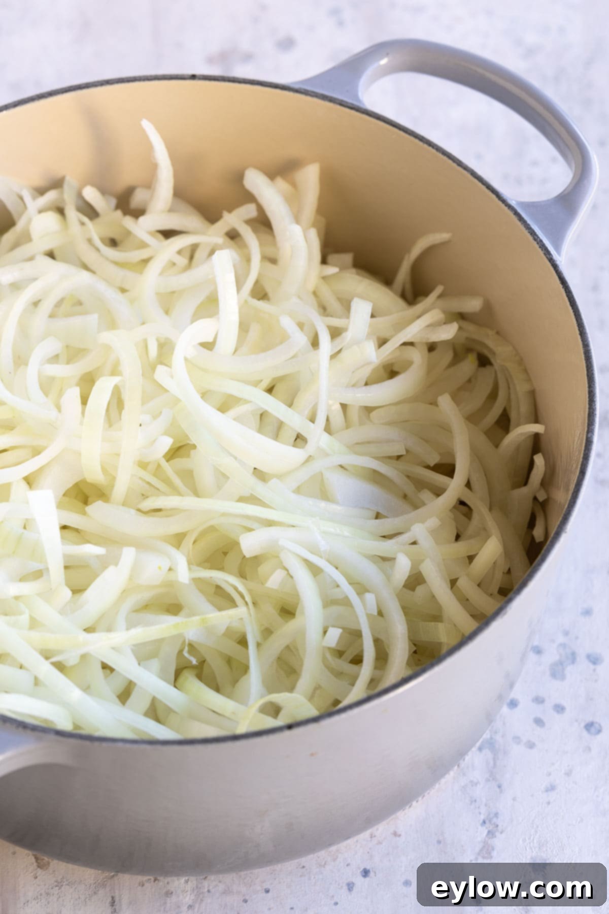 Effortless French Onion Soup 3 A gray dutch oven filled with thinly sliced white onions for soup, ready for caramelization.