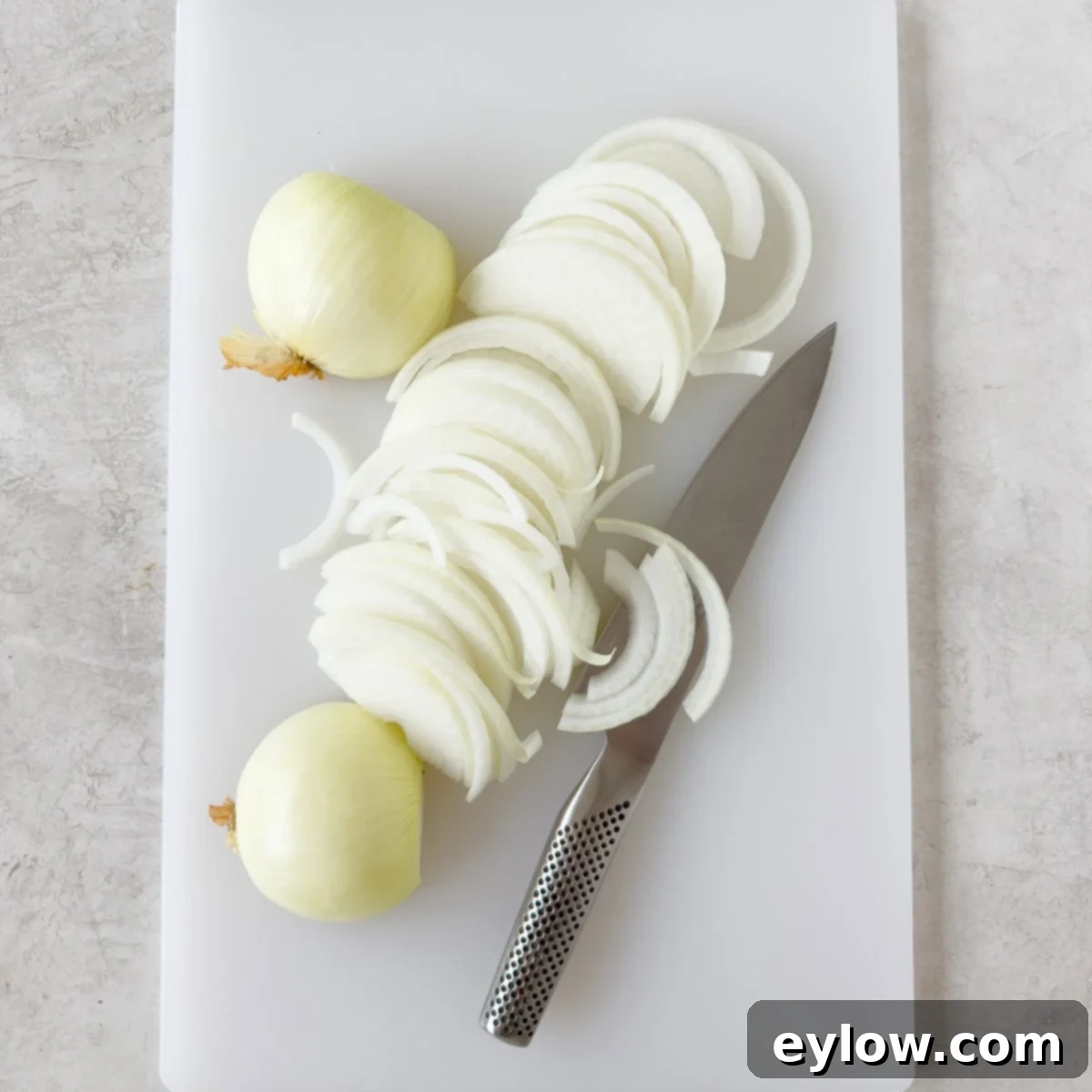 Process of cutting onions for French Onion Soup Slicing onions for French onion chicken on a white cutting board, demonstrating uniform cuts.